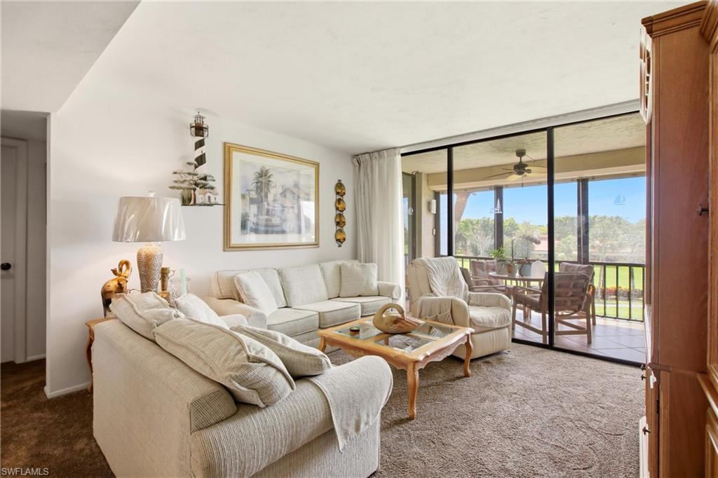 Living area with broad sliding glass doors opening to a screened balcony, featuring a ceiling fan and tiled flooring