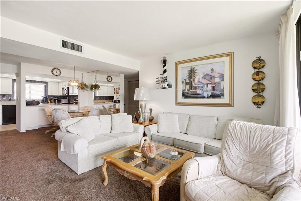 Open-concept living area featuring wall-to-wall carpeting and a kitchen with white cabinetry, black appliances, and a tiled backsplash
