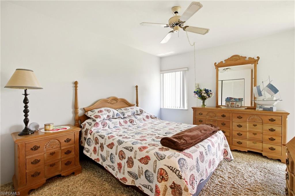 Carpeted bedroom featuring a window with vertical blinds, a ceiling fan, and light-toned walls