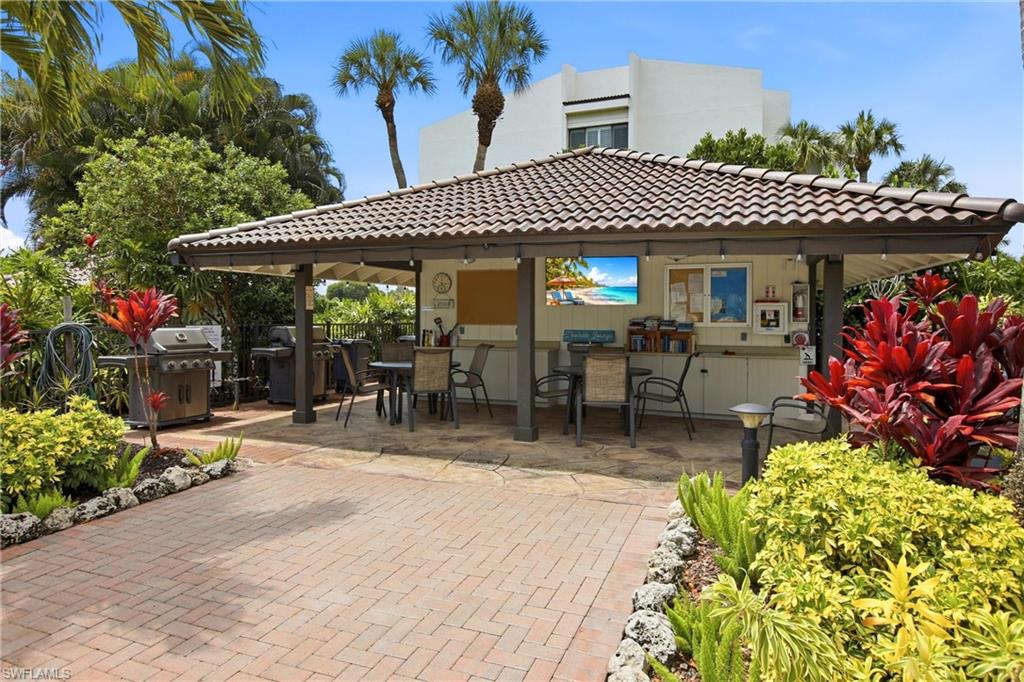 Outdoor pavilion with a tiled roof, integrated bar area, built-in cabinetry, dual grills, and lush surrounding landscaping