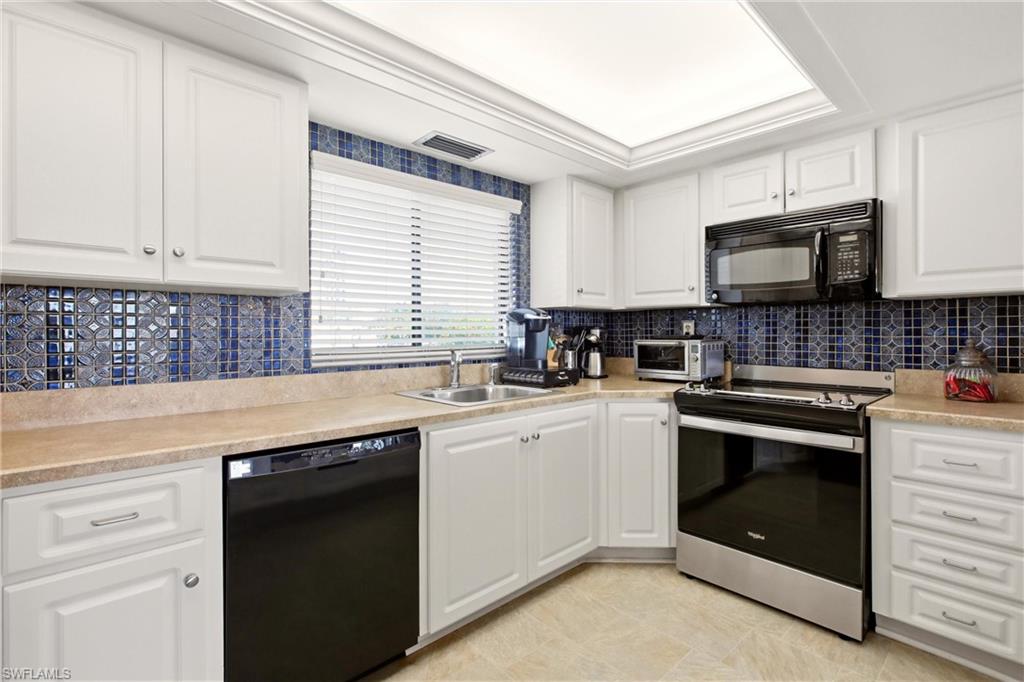 Kitchen featuring white cabinetry, blue mosaic tile backsplash, light-toned countertops, and stainless steel sink