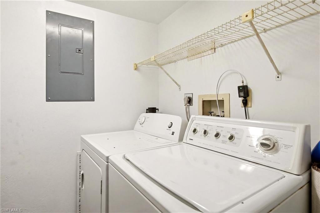 Dedicated laundry area featuring a white top-load washing machine and dryer, a wall-mounted wire shelving unit, and an electrical panel