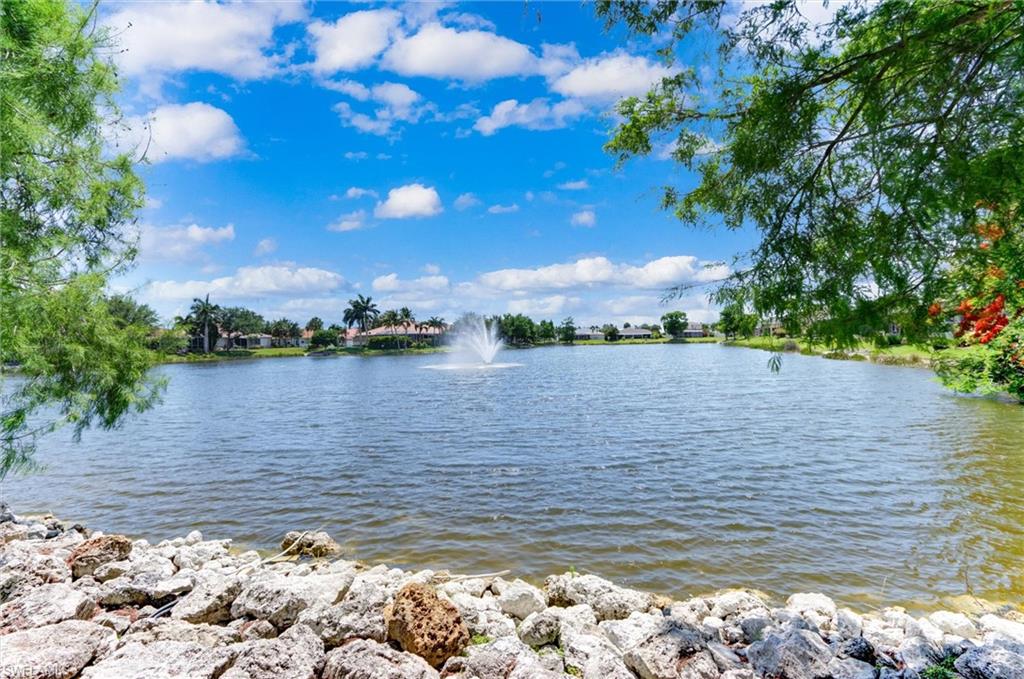Waterfront setting featuring a fountain, surrounding foliage, and a rocky shoreline