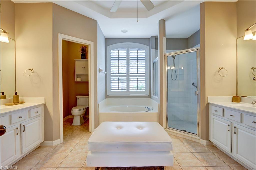 Dual vanity with integrated sinks, a built-in soaking tub with plantation shutters, a glass-enclosed shower, and tile flooring