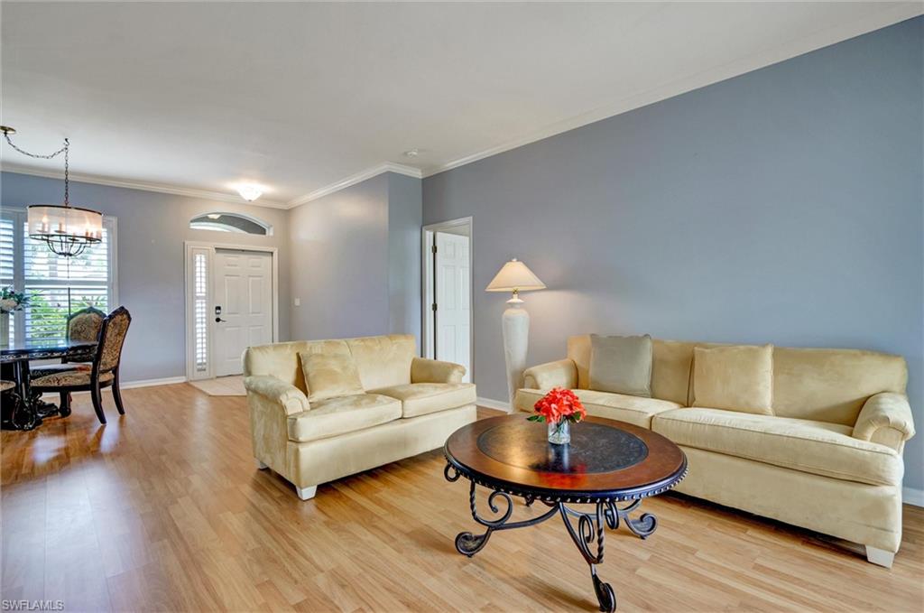 Wood-finish flooring, crown molding, arched entryway, window with horizontal blinds, and a decorative chandelier