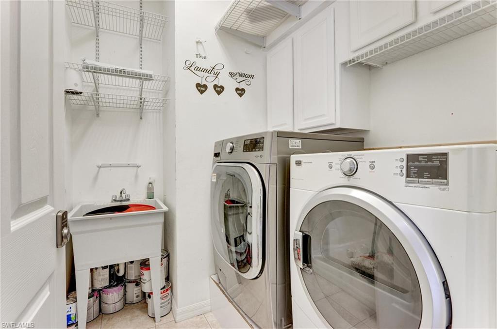 Utility sink with faucet, white wall-mounted shelving, overhead cabinetry, and tile flooring