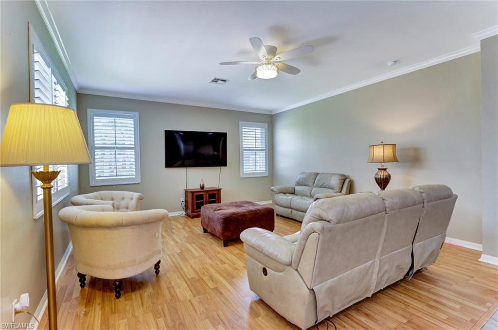 Recessed wall-mounted television, wood-finish flooring, white louvered window treatments, crown molding, and a ceiling fan with integrated lighting
