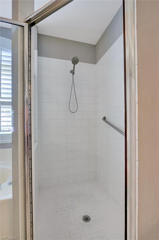 Shower enclosure with white tiled walls, a floor drain, and a wall-mounted showerhead