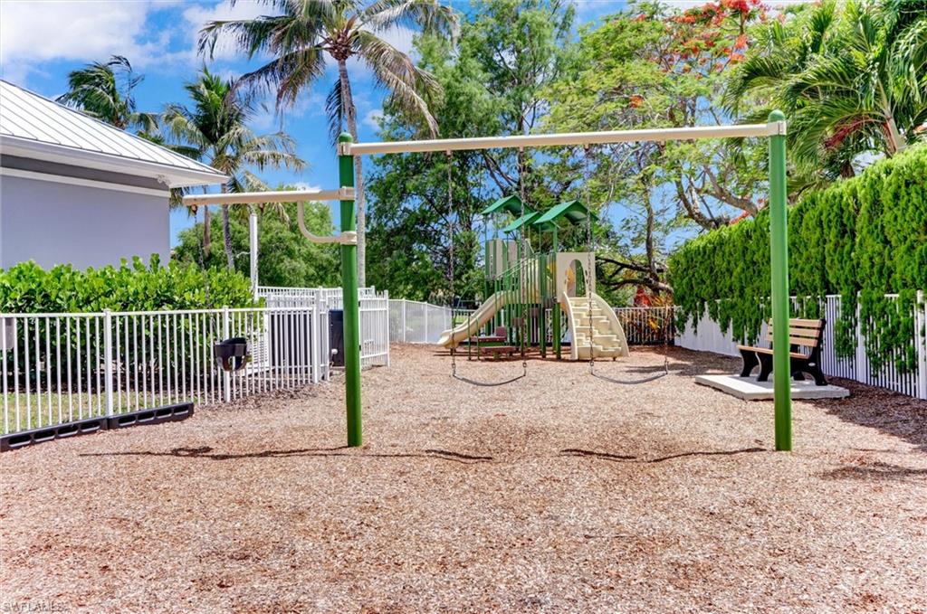 Playground area featuring a swing set, slide structure, protective ground covering, and perimeter fencing
