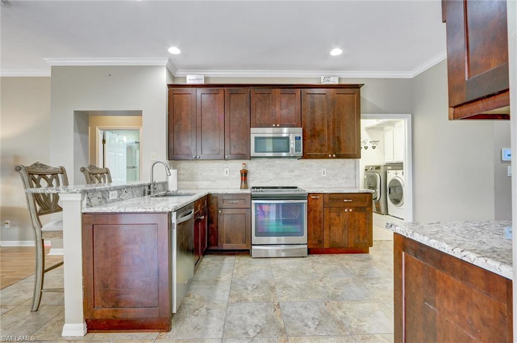 Kitchen featuring wood cabinetry, light-toned stone countertops, stainless steel appliances, and a tile backsplash