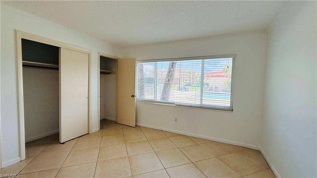 Tile flooring, two closet spaces with sliding doors, a window with blinds, and white painted walls