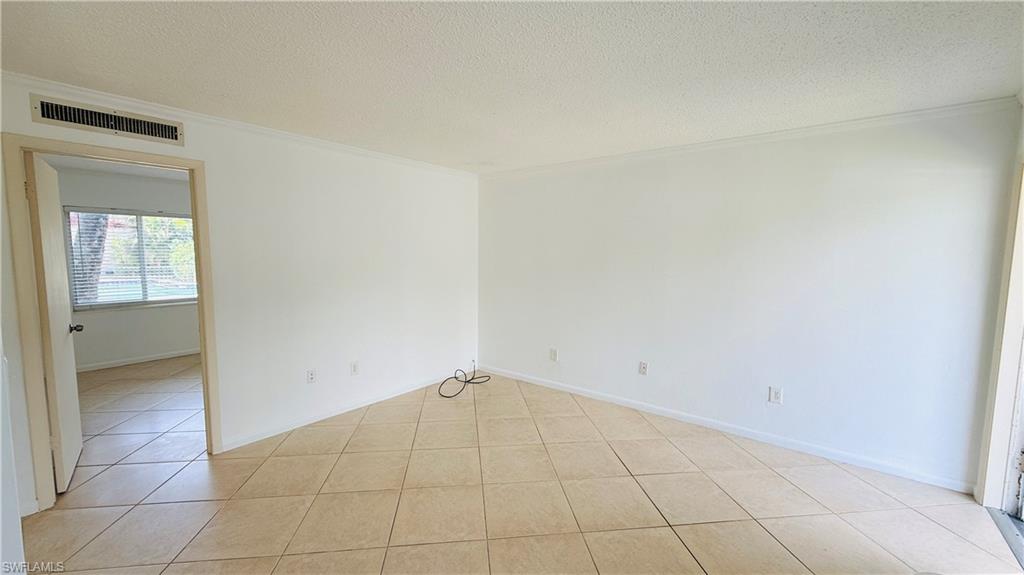 Light-colored diagonal tile flooring, white painted walls, crown molding, and a visible doorway leading to another room with a window