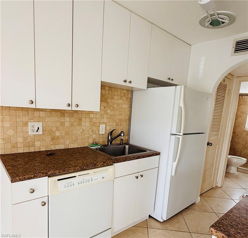 White cabinetry, mosaic tile backsplash, integrated dishwasher, double basin sink, and archway with louvered door