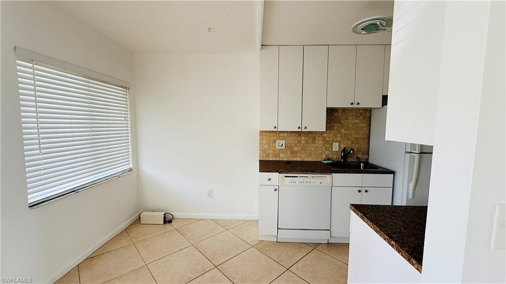 Kitchen featuring white cabinetry, a dark countertop, a mosaic tile backsplash, and a built-in dishwasher