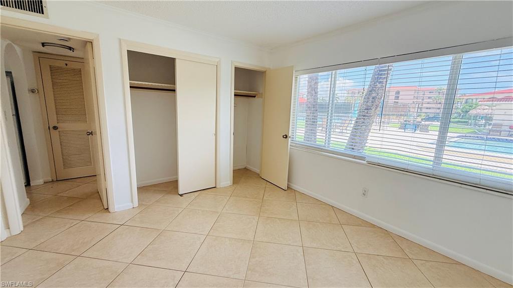 Tile flooring throughout, white painted walls, large window with horizontal blinds, and two integrated closets with bi-fold doors