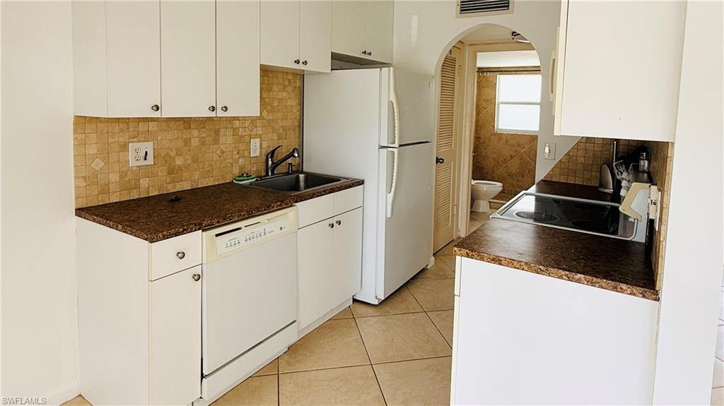 White cabinetry, tile backsplash, built-in dishwasher, and a stainless steel sink