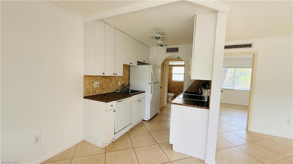 Kitchen featuring white cabinetry, granite-style countertops, mosaic tile backsplash, stainless steel sink, and white appliances