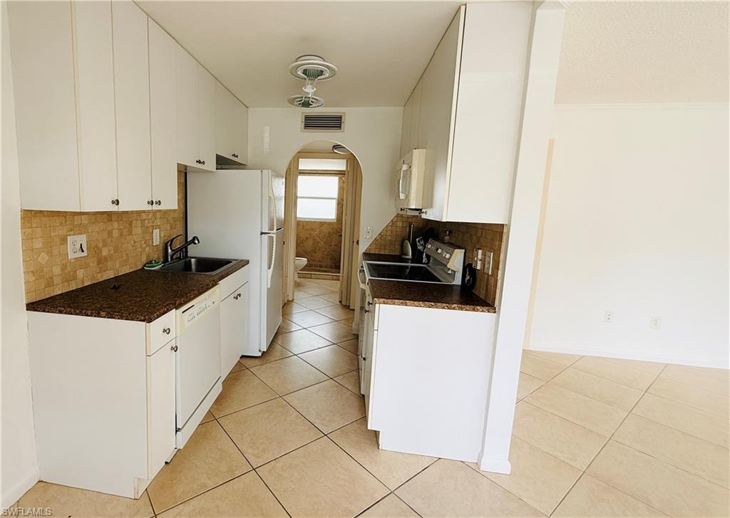 Kitchen featuring white cabinetry, dark speckled countertops, a tile backsplash, and tile flooring