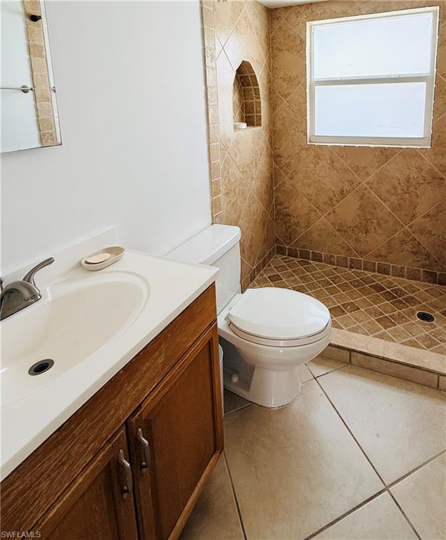 Ceramic tile flooring, vanity with wood-finish cabinetry, integrated sink, and a tiled shower with a built-in niche