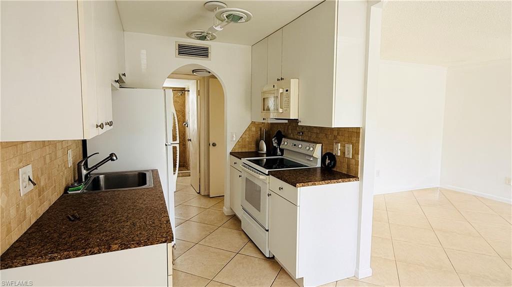 Kitchen featuring white cabinetry, brown speckled countertops, mosaic tile backsplash, and stainless steel sink