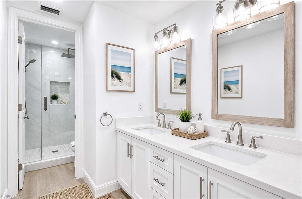 Virtual Renovation: Dual vanity with integrated sinks and quartz countertops, white cabinetry with brushed nickel hardware, two framed mirrors, and a glass-enclosed shower with a recessed niche