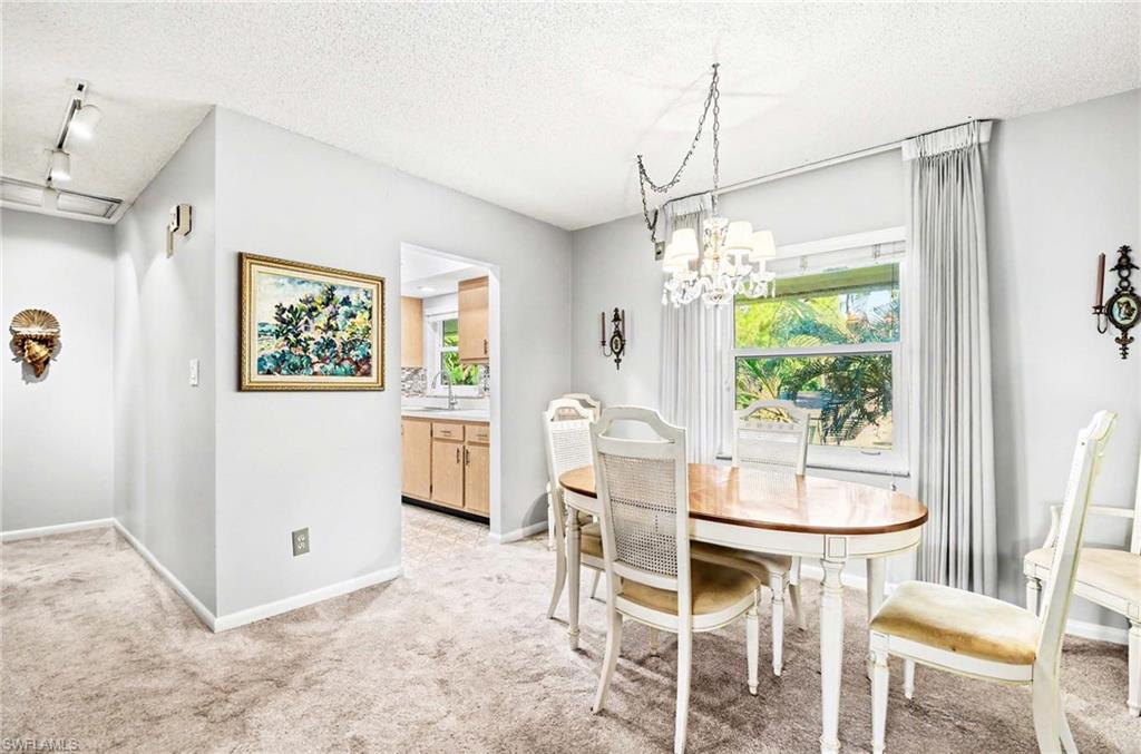 Dining area with a chandelier and window, complemented by light-colored carpeting and pale gray walls
