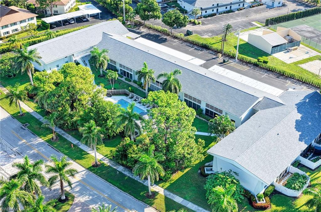 Building complex featuring a central swimming pool, lush landscaping, and a paved parking area