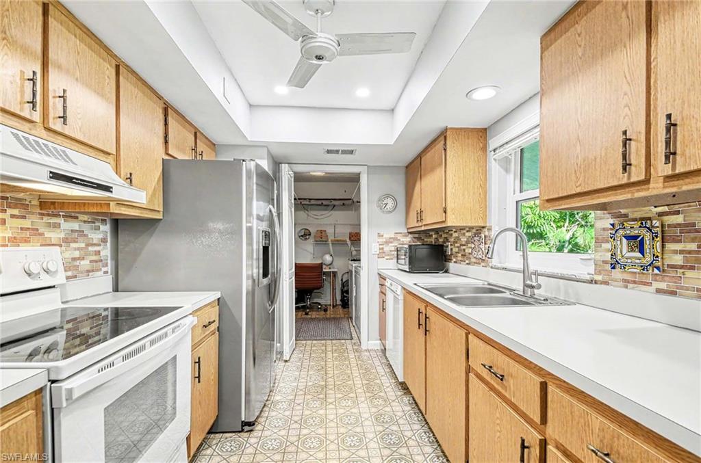 Galley kitchen featuring wood cabinetry, white countertops, a mosaic tile backsplash, a dual basin stainless steel sink, and stainless steel appliances