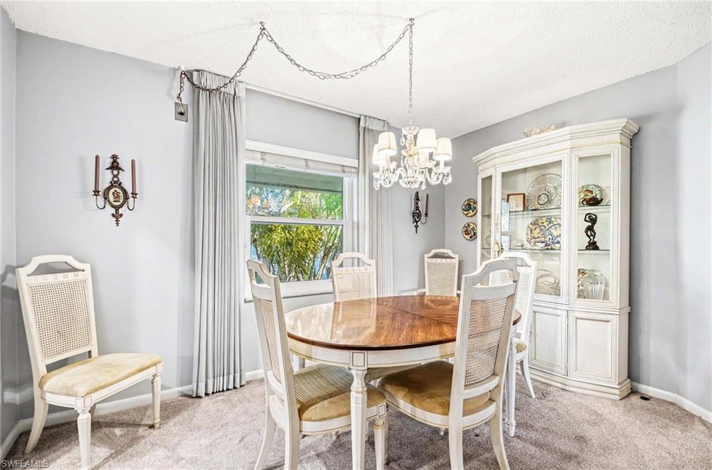 Built-in display cabinet with glass doors, chandelier lighting, wall sconces, window with drapes, and carpeted flooring