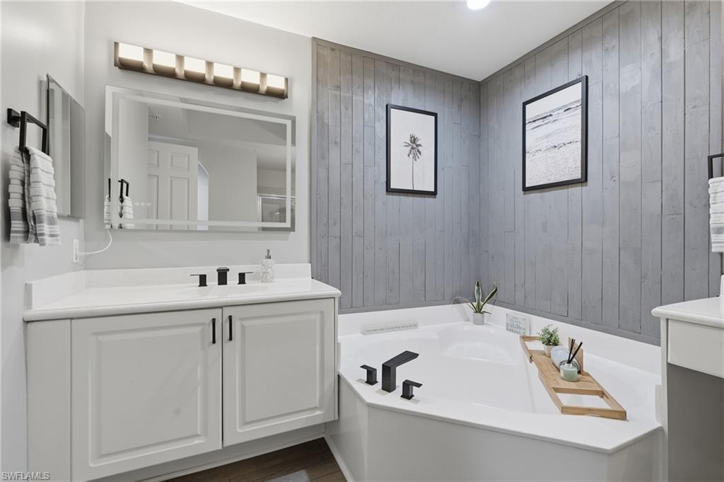 Corner soaking tub with a matte black faucet, vanity with a white countertop, and textured wall paneling