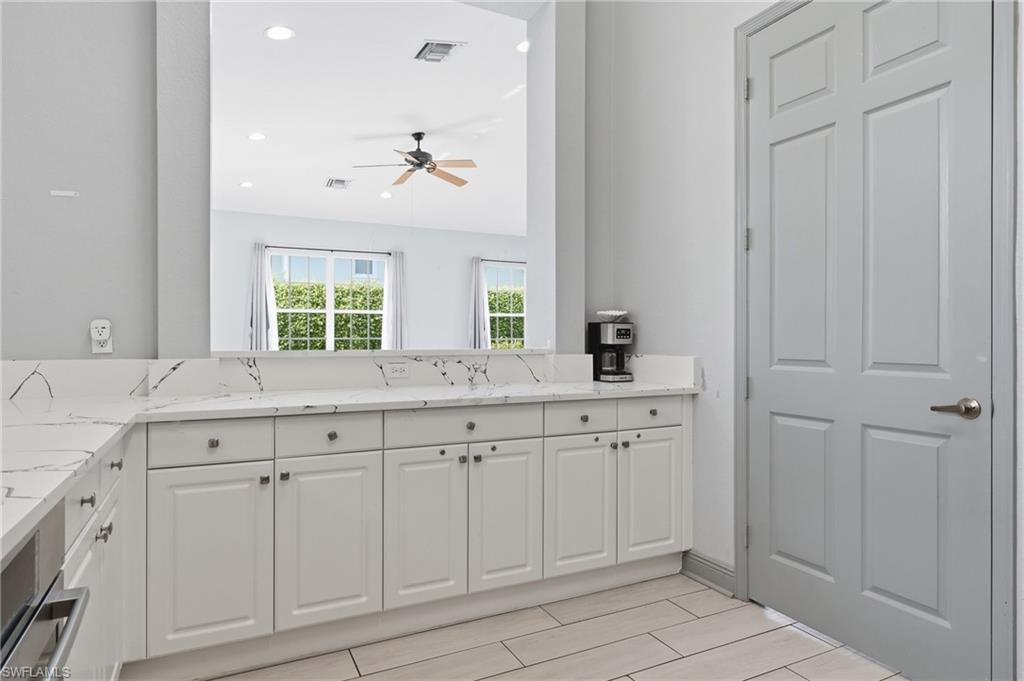 Kitchen located in side community room of clubhouse.  Kitchen featuring white cabinetry, stainless steel appliances, white countertops with dark veining, and an arched window