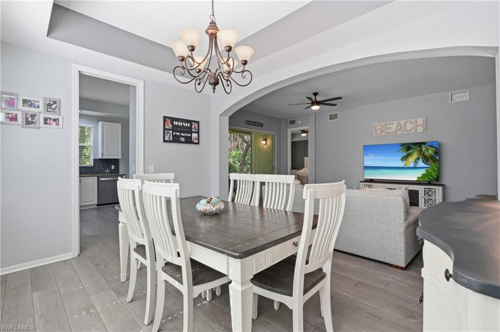 Tray ceiling with chandelier, light wood-finish flooring, arched doorway, and recessed kitchen with white cabinetry