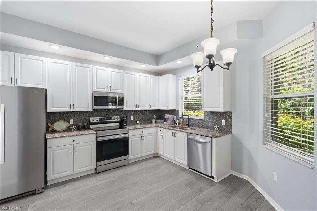 Kitchen featuring white cabinetry, stainless steel appliances, speckled countertops, and wood-finish flooring