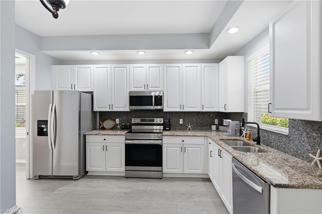 Kitchen featuring white shaker-style cabinetry, stainless steel appliances, granite countertops, and a dark mosaic tile backsplash