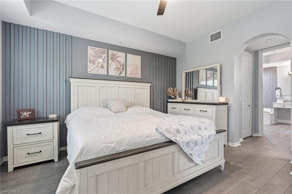 Wood-finish flooring, accent wall with vertical paneling, arched doorway, and ceiling fan