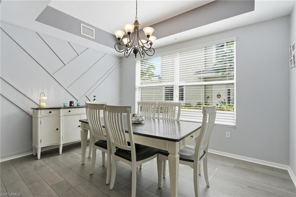 Accent wall with geometric paneling, wood-finish flooring, chandelier lighting, and a large window with blinds