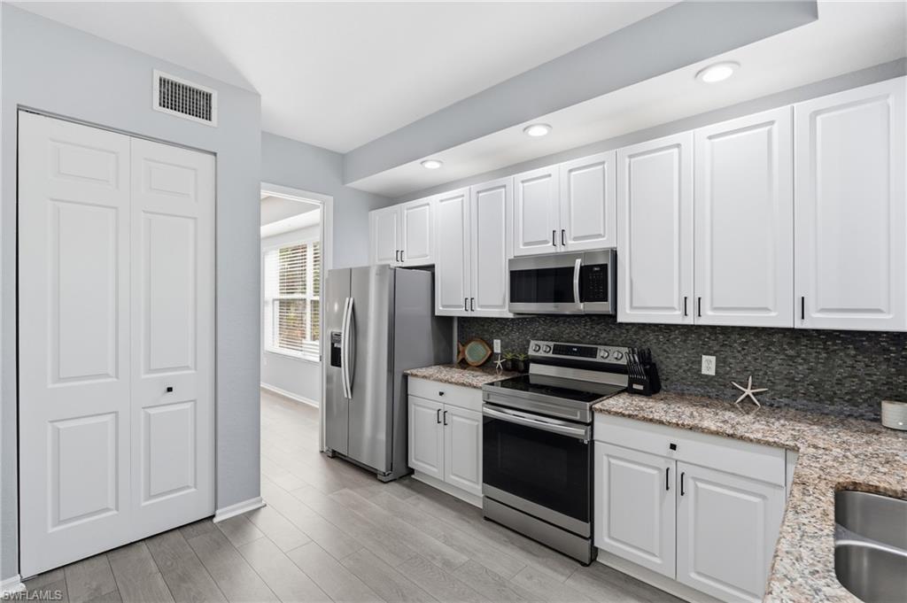 Modern kitchen featuring white shaker-style cabinetry, stainless steel appliances, granite countertops, and a mosaic tile backsplash