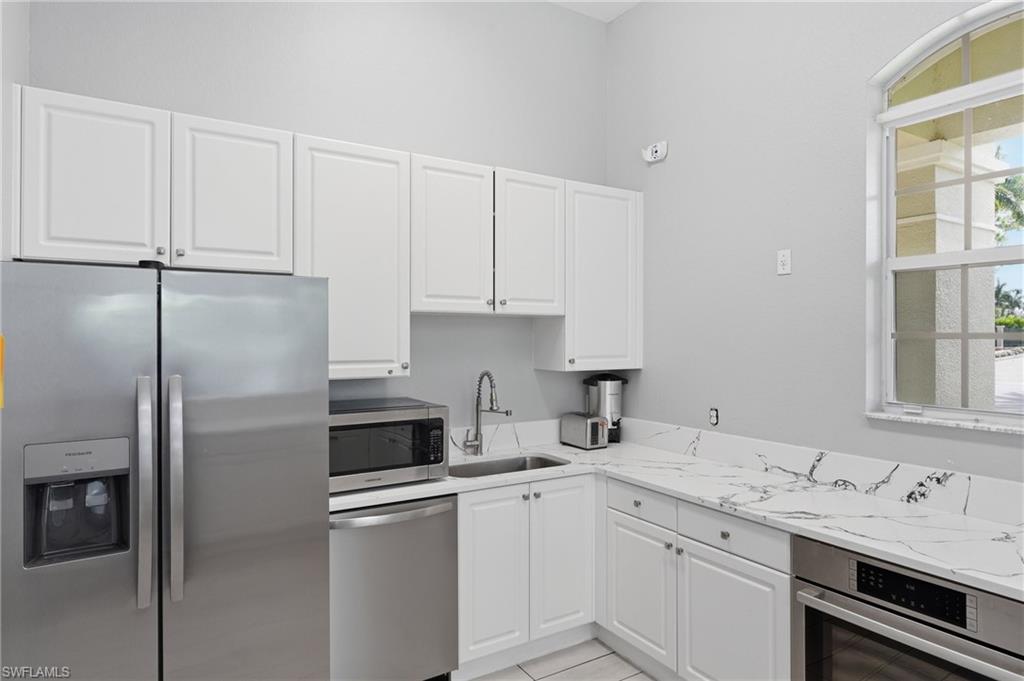 White cabinetry, stainless steel appliances, corner sink, white countertops with prominent veining, and an arched window