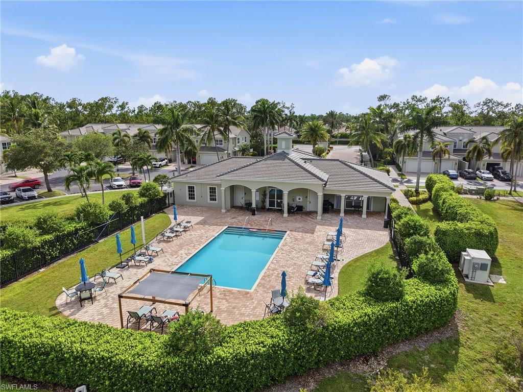 Community pool with a paver deck, covered lounge area, and manicured hedges