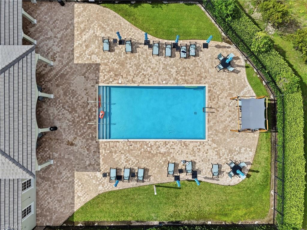 Rectangular swimming pool surrounded by a large paver patio, bordered by green lawn and mature landscaping