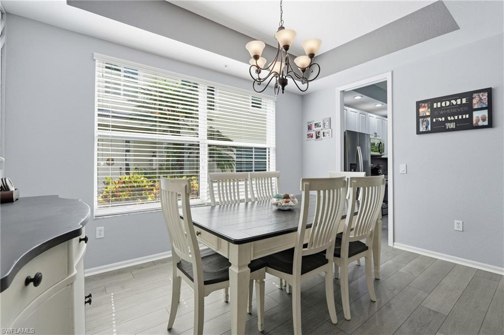 Recessed ceiling detail, contemporary chandelier, large window with blinds, wood-finish flooring, and a built-in cabinetry with a dark countertop