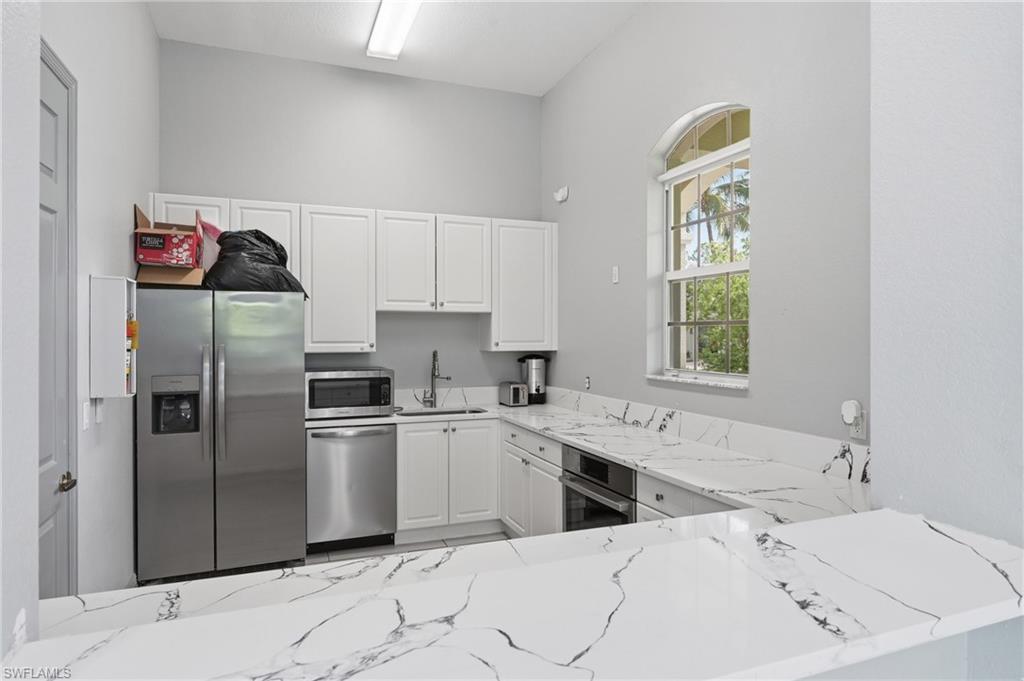 Kitchen located in side community room of clubhouse.  Kitchen featuring white cabinetry, stainless steel appliances, white countertops with dark veining, and an arched window