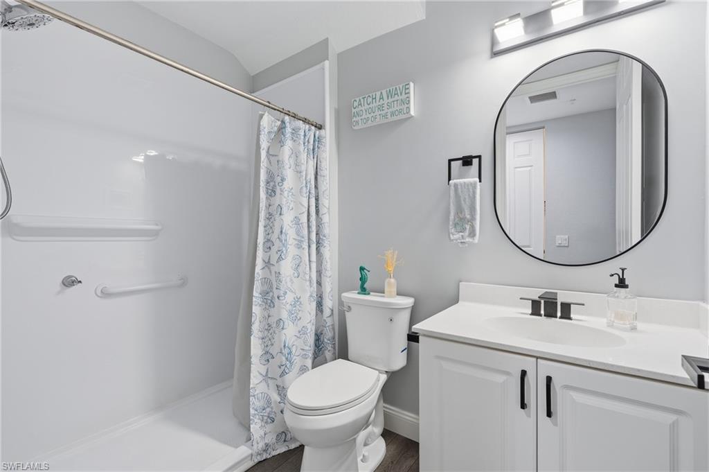 White vanity with a rectangular basin sink and matte black faucet, wall-mounted oval mirror, and a white shower stall with an integrated shelf
