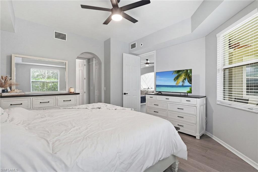 Light grey walls, wood-finish flooring, ceiling fan with integrated lighting, arched doorway, and built-in white dresser with dark countertop