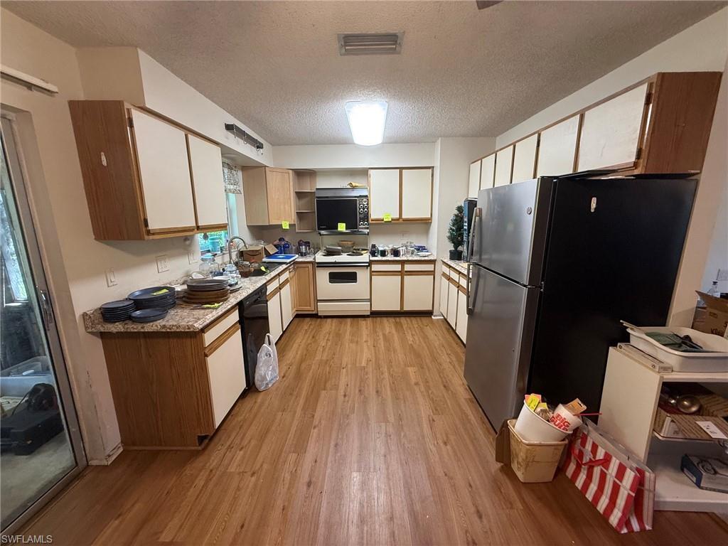 Kitchen featuring wood-finish flooring, L-shaped cabinetry with wood-tone bases and white upper doors, stainless steel refrigerator, white electric range, and light-toned countertops