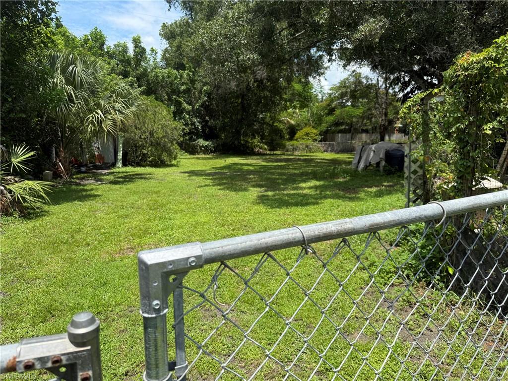 Expansive green space featuring a chain-link fence, mature trees, and natural landscaping