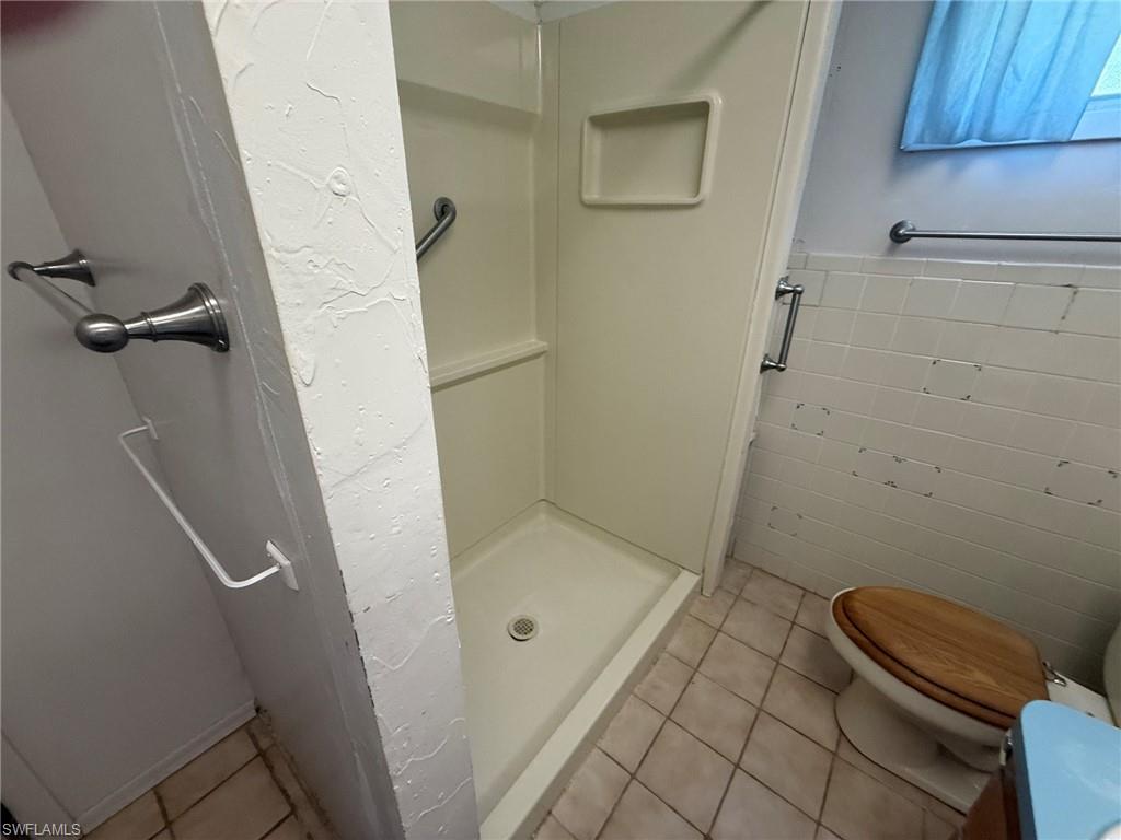 Shower stall with integrated soap dish, chrome grab bars, and a neutral-toned tile floor