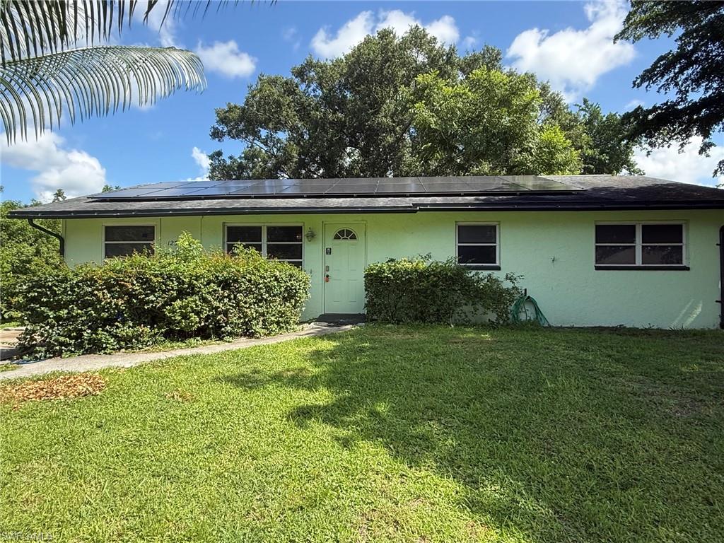 Light green exterior with a black roof, solar panels, and mature landscaping