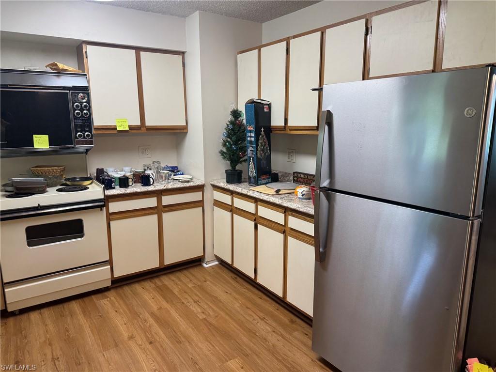 Wood-finish flooring, white cabinetry with wood trim, light-toned countertops, wall-mounted microwave, and a stainless steel refrigerator