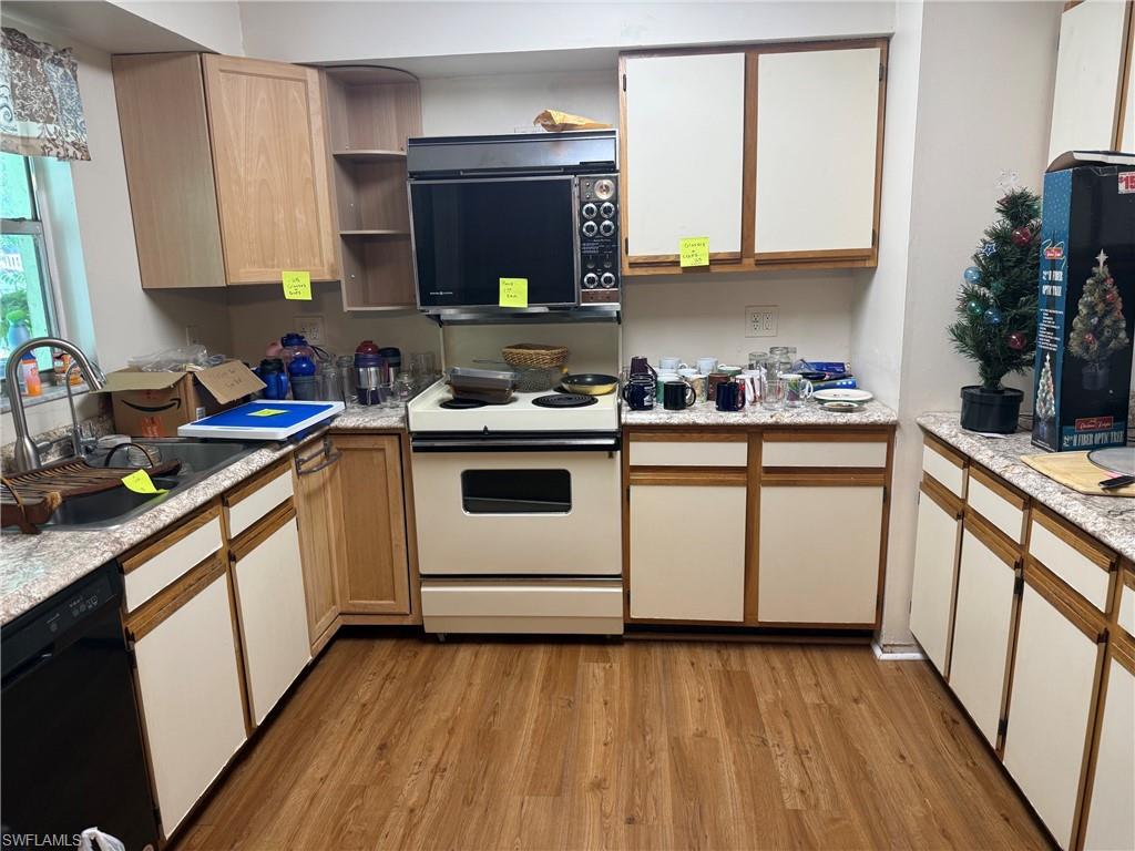 U-shaped kitchen featuring wood-finish flooring, light-toned cabinetry with contrasting wood trim, light-toned countertops, and a built-in wall oven